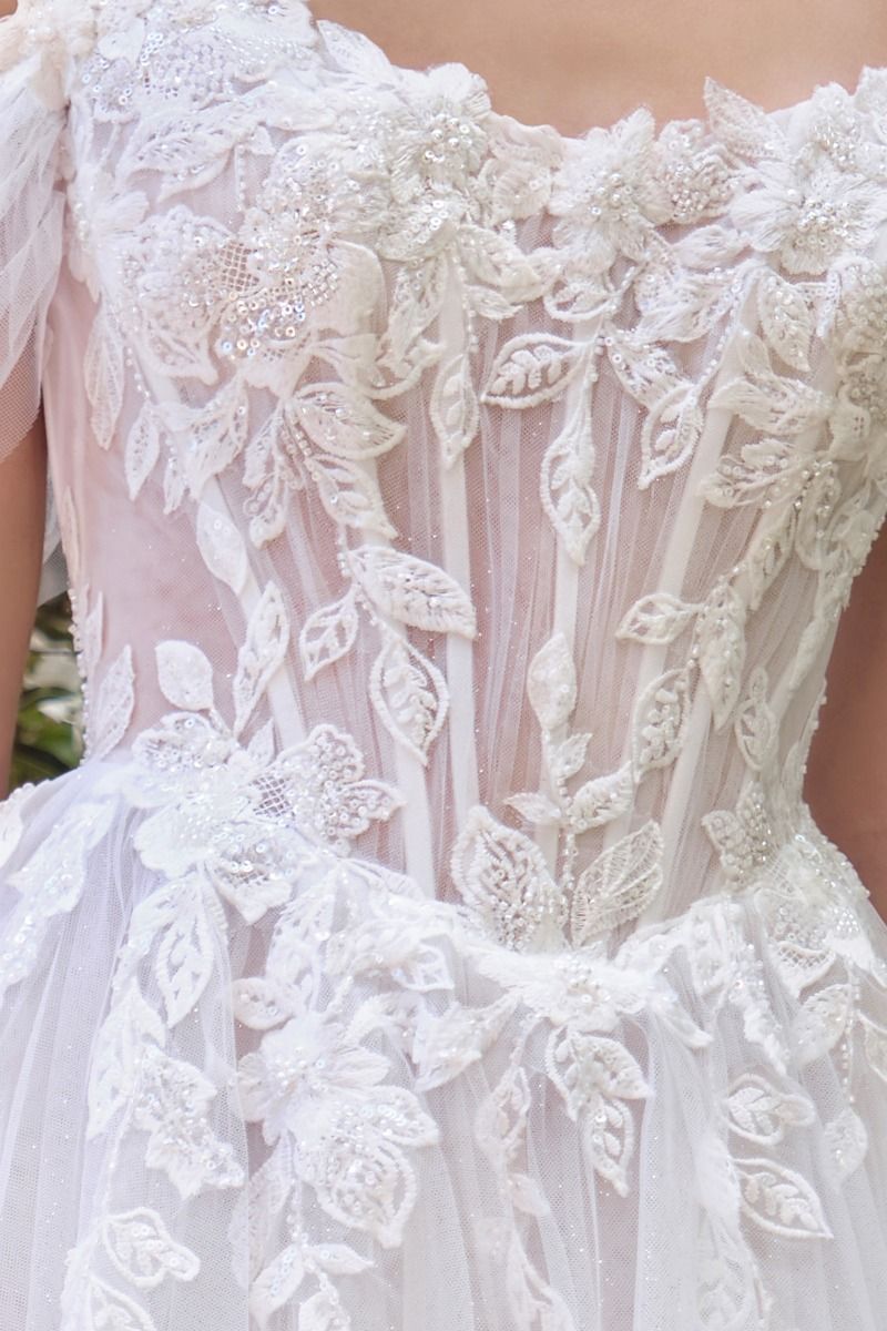 Vestido de Novia Escote ilusión con hombros descubiertos, apliques florales y mangas drapeadas transparentes.