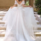 Vestido de Novia Escote ilusión con hombros descubiertos, apliques florales y mangas drapeadas transparentes.